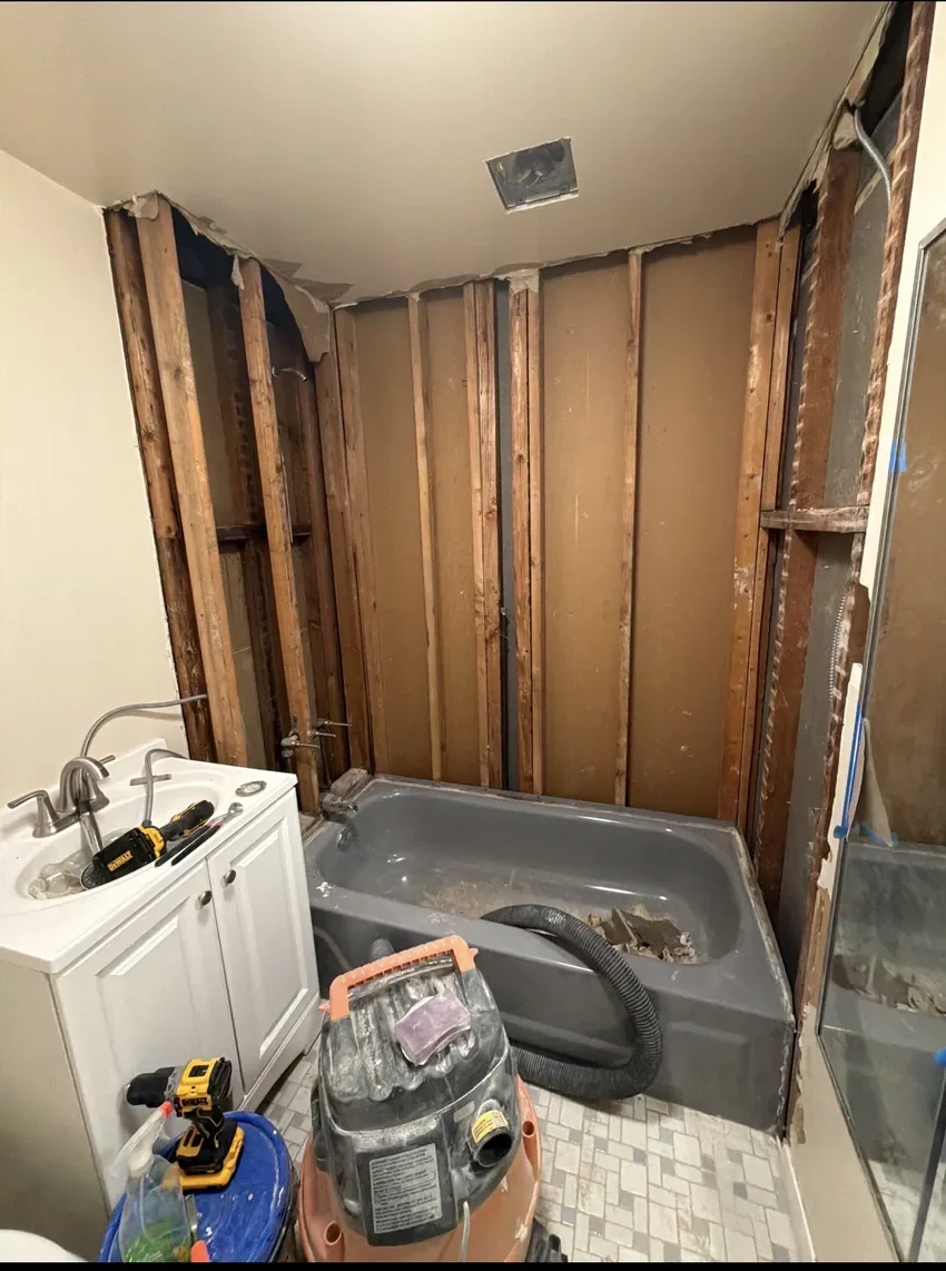 Before: Bathroom during renovation with exposed wall studs, construction equipment, and old tub