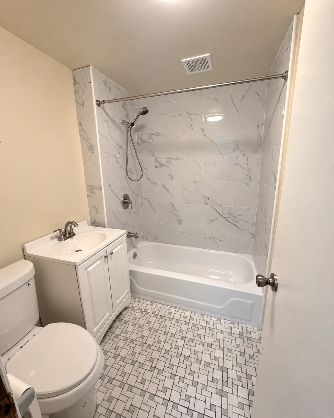 After: Renovated bathroom featuring a white bathtub and marble-look wall tile with no shower curtain